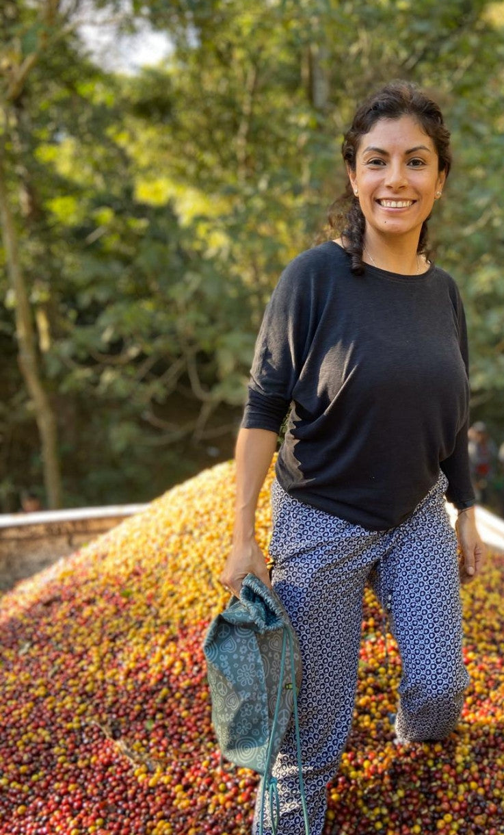 Woman standing on a hill covered with coffee beans, with a crowd in the background.